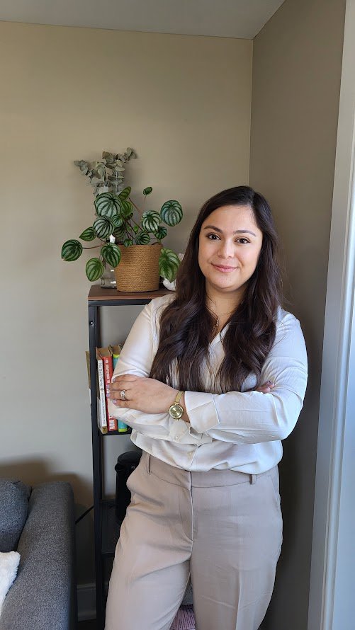 Aya El Balaa, Registered Psychotherapist, standing beside a plant, signifying a calm, open presence